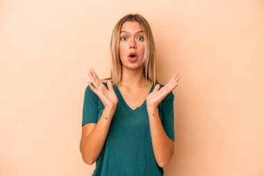 Beyaz tenli genç bir kadın bej arka planda izole edilmiş. Şaşırmış ve şok olmuş..