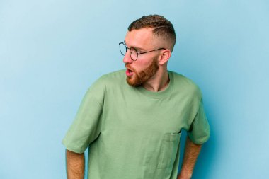 Mavi arka planda soyutlanmış genç beyaz bir adam gülümsüyor, neşeli ve keyifli görünüyor..