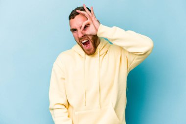 Kafkasyalı genç adam mavi arka planda izole edildi. Heyecanlı görünüyor..