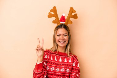 Young caucasian woman wearing a christmas reindeer hat isolated on beige background showing number two with fingers.