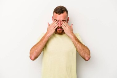 Beyaz arka planda izole edilmiş genç beyaz bir adam elleriyle gözlerini kapatmaktan korkuyor..