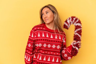 Kafkasyalı genç bir kadın sarı arka planda izole edilmiş büyük bir Noel sopası tutuyor. Amaçlarına ve amaçlarına ulaşma hayali kuruyor.