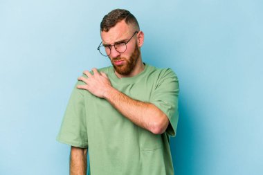 Mavi arka planda izole edilmiş, omuz ağrısı olan genç beyaz bir adam..