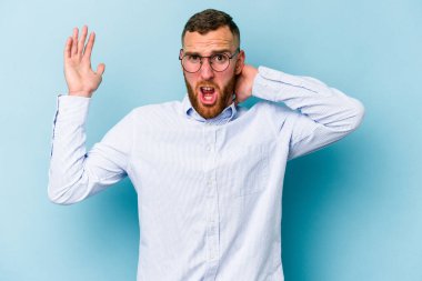 Mavi arka planda izole edilmiş genç beyaz adam öfkeyle bağırıyor..