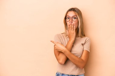 Beyazlı genç bir kadın bej arka planda izole edilmiş. Yan tarafı işaret ediyor.