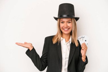 Young caucasian wizard woman holding magic card isolated on white background showing a copy space on a palm and holding another hand on waist.