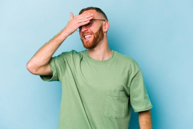 Mavi arka planda izole edilmiş genç beyaz adam ellerini başının üstünde tutarak neşe içinde gülüyor. Mutluluk kavramı.