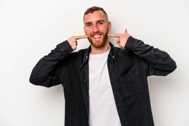 Beyaz arka planda izole edilmiş genç beyaz adam gülümsüyor, parmaklarını ağıza doğrultuyor..