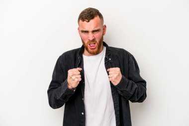 Beyaz arka planda izole edilmiş genç beyaz bir adam yumruğunu kameraya gösteriyor, agresif bir yüz ifadesi..