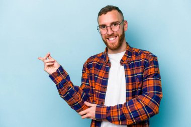 Mavi arka planda izole edilmiş genç beyaz adam işaret parmağıyla işaret ederek gülümsüyor..