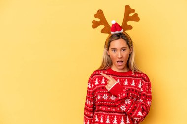 Young caucasian woman wearing a christmas reindeer hat isolated on beige background pointing to the side