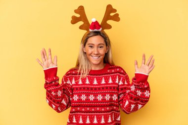 Young caucasian woman wearing a christmas reindeer hat isolated on beige background receiving a pleasant surprise, excited and raising hands.