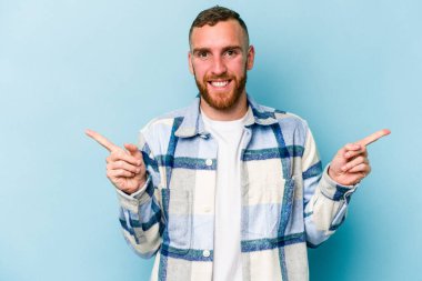 Mavi arka planda izole edilmiş genç beyaz adam farklı kopya alanlarını gösteriyor, birini seçiyor, parmaklarıyla gösteriyor.