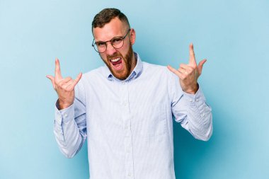 Mavi arka planda izole edilmiş genç beyaz adam boynuzlarını devrim konsepti olarak gösteriyor..