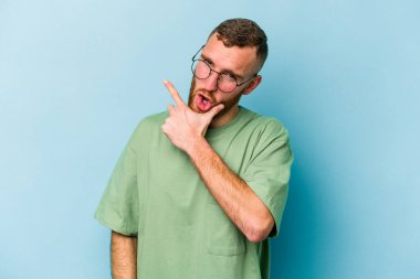 Kafkasyalı genç bir adam mavi arka planda izole edilmiş. Bir strateji planlıyor, bir iş yolu düşünüyor..