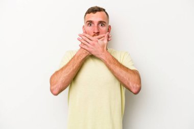 Beyaz arka planda izole edilmiş genç beyaz adam elleriyle ağzını kapatırken şok oldu..