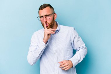 Mavi arka planda izole edilmiş genç beyaz bir adam ya sır saklıyor ya da sessizlik istiyor..