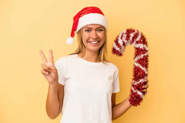 年轻的高加索女人手里拿着大的圣诞棒 被黄色背景隔离 手指头伸出二号 — 图库照片