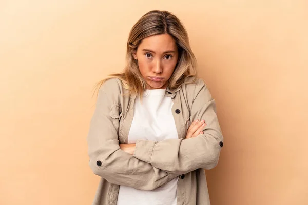 Young caucasian woman isolated on beige background blows cheeks, has tired expression. Facial expression concept.