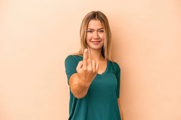 Young caucasian woman isolated on beige background pointing with finger at you as if inviting come closer.