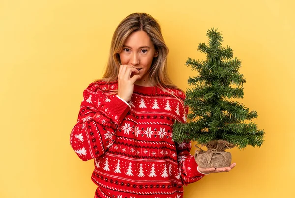 Mladá Běloška Drží Malý Vánoční Stromek Izolované Žlutém Pozadí Kousání — Stock fotografie