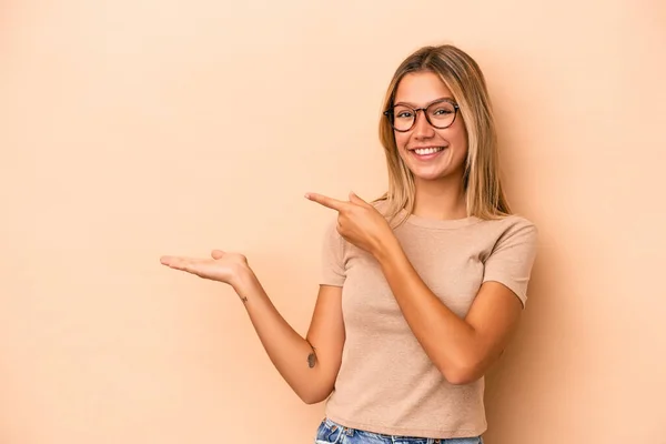 Joven Mujer Caucásica Aislada Sobre Fondo Beige Excitada Sosteniendo Espacio —  Fotos de Stock