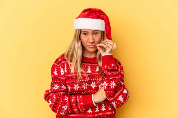 年轻的高加索女人用手指捂着嘴唇保守秘密 在黄色背景下庆祝圣诞节 — 图库照片