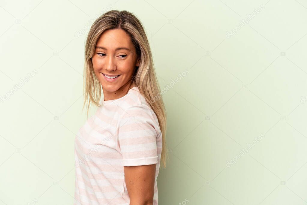 Young caucasian woman isolated on green background looks aside smiling, cheerful and pleasant.
