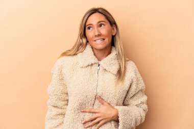 Beyaz tenli genç bir kadın bej arka planda izole edilmiş karnına dokunuyor, nazikçe gülümsüyor, yemek yiyor ve tatmin oluyor..