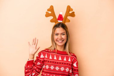Young caucasian woman wearing a christmas reindeer hat isolated on beige background smiling cheerful showing number five with fingers.