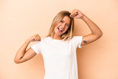 Beyaz tenli genç bir kadın, bej arka planda izole edilmiş özel bir günü kutluyor, atlıyor ve enerji ile kollarını kaldırıyor..