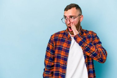 Mavi arka planda izole edilmiş genç beyaz bir adam gizli bir sıcak fren haberi veriyor ve yana bakıyor.