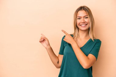 Beyazlı genç bir kadın bej arka planda izole edilmiş. İşaret parmaklarıyla işaret ettiği için heyecanlı..