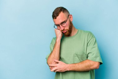 Mavi arka planda izole edilmiş, üzgün ve dalgın hisseden, kopyalama alanına bakan genç beyaz bir adam..