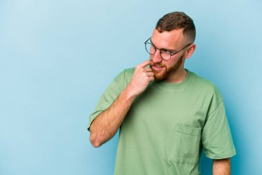 Mavi arka planda izole edilmiş genç beyaz adam rahatlamış bir şeyin fotokopi odasına baktığını düşünüyor..