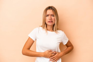 Beyaz tenli, bej arka planda izole edilmiş genç bir kadın. Karaciğer ağrısı, karın ağrısı var..