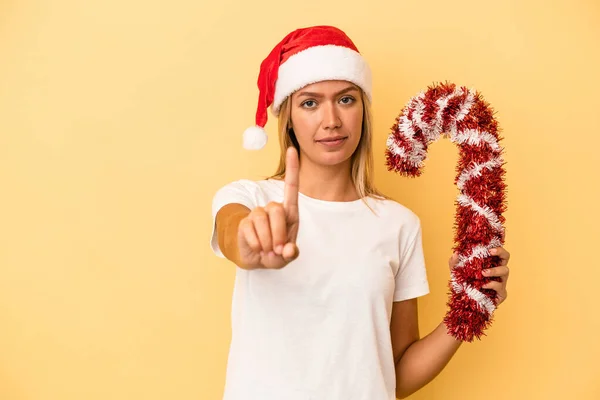 年轻的高加索女人手里拿着大的圣诞棒 被黄色背景隔离 带着第一个手指 — 图库照片