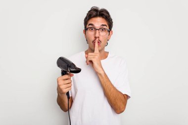 Beyaz arka planda izole edilmiş saç kurutma makinesi tutan genç İspanyol bir adam ya sır saklıyor ya da sessizlik istiyor..