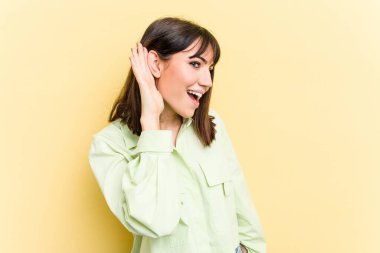 Sarı arka planda izole edilmiş genç beyaz kadın bir dedikoduyu dinlemeye çalışıyor..