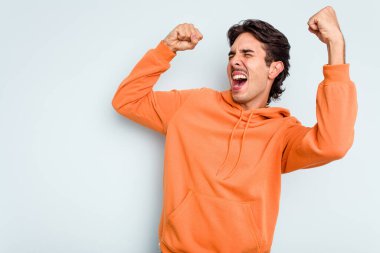 Mavi arka planda izole edilmiş genç İspanyol bir adam zaferden sonra yumruk kaldırıyor, kazanan konsept..