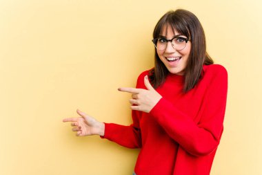 Sarı arka planda izole edilmiş genç beyaz kadın işaret parmağıyla işaret ederek heyecanlanıyor..