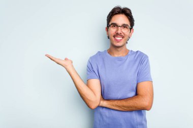 Mavi arka planda izole edilmiş genç İspanyol bir adam avucunun içinde bir fotokopi alanı ve belinde bir el daha gösteriyor..