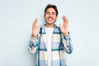 Genç İspanyol adam mavi arka planda izole edilmiş neşeli bir şekilde gülüyor. Mutluluk kavramı.