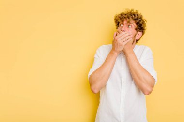 Kafkasyalı genç adam sarı arka planda izole edilmiş. Düşünceli bir şekilde, ağzını eliyle kapatan bir fotokopi odasına bakıyor..
