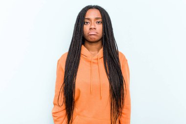 Saçları mavi arka planda izole edilmiş genç Afrikalı Amerikalı kadın üzgün, ciddi yüz, sefil ve hoşnutsuz hissediyor..