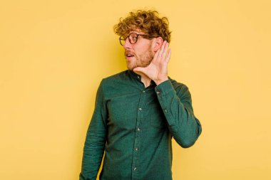 Sarı arka planda izole edilmiş genç beyaz bir adam bir dedikoduyu dinlemeye çalışıyor..