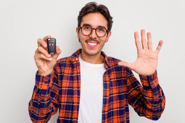 Beyaz arka planda izole edilmiş araba anahtarlarını tutan İspanyol genç adam gülümseyerek beş numarayı parmaklarıyla gösteriyor..