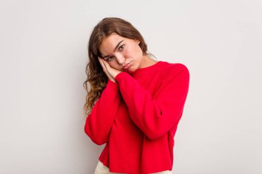 Mavi arka planda izole edilmiş genç beyaz kadın esniyor. Ağzı eliyle kapatan yorgun bir hareket sergiliyor..