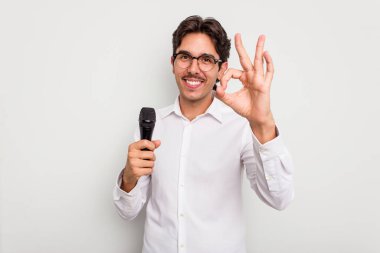 Genç İspanyol şarkıcı beyaz arka planda izole edilmiş neşeli ve kendinden emin bir şekilde iyi bir jest yapıyor..