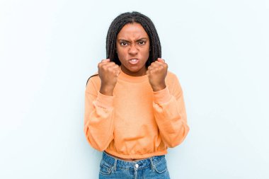 Mavi arka planda saç örgüsü olan genç Afrikalı Amerikalı kadın kameraya yumruk gösteriyor, agresif yüz ifadesi var..